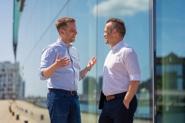 Two men talking to each other in front of a glass building in Copenhagen